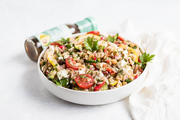 Gluten-free Lemon Orzo Salad in a white bowl, with a bottle of Primal Kitchen dressing in the background.