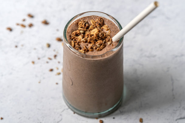 A chocolate protein smoothie made with Primal Kitchen Collagen Fuel, in a clear glass. 