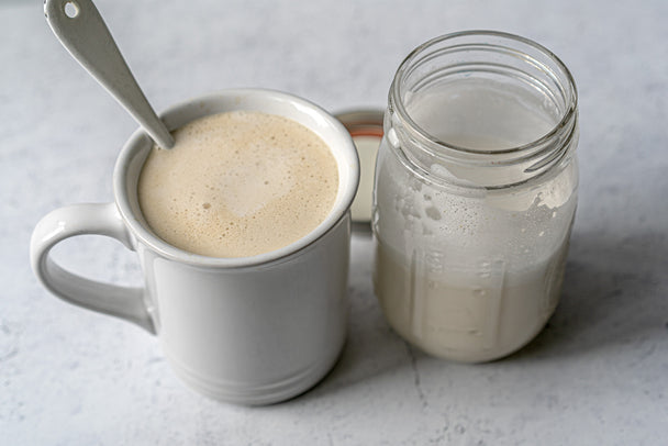 A jar of Vanilla Coconut Collagen Creamer next to a cup of coffee with creamer stirred into it. 