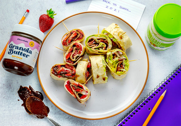 A plate of sweet and savory pinwheel sandwiches with a jar of Primal Kitchen Mayo, notebook, and a jar of granola butter in the background. 