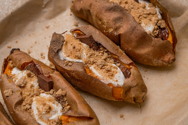 Three grilled sweet potatoes on a baking sheet, topped with gooey homemade marshmallows, chocolate, and graham cracker crumbs. 