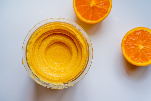 Overhead shot of no-dairy orange sorbet in a clear container, with sliced orange halves in the background. 