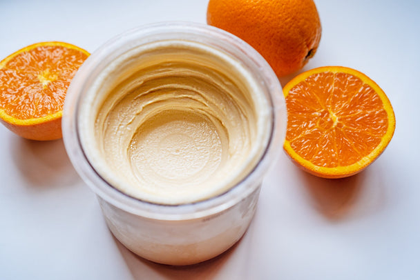 Overhead view of creamy vanilla orange sherbet in a clear container with sliced fresh orange halves in the background. 