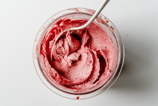 Overhead shot of creamy fruit sorbet in a clear container, with a spoon dipped into the sorbet.  