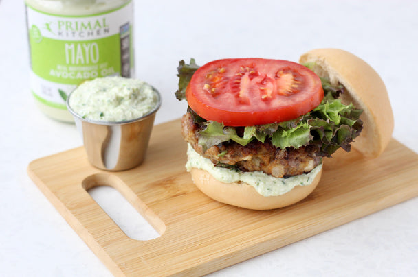 A juicy open-face lamb burger on a cutting board with a small metal container of feta mayo and a jar of Primal Kitchen Mayo.   