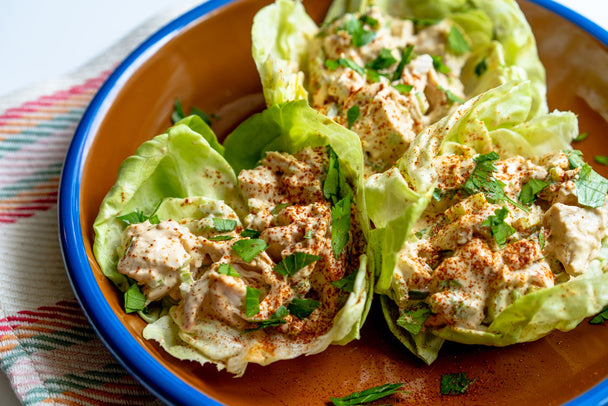 Three lettuce wraps filled with Chipotle Lime Chicken Salad on a red and blue plate, with a striped napkin underneath..