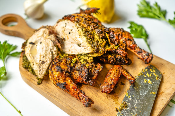 A whole roasted chicken marinated in Green Goddess dressing on a wooden cutting board, with a knife and herbs.