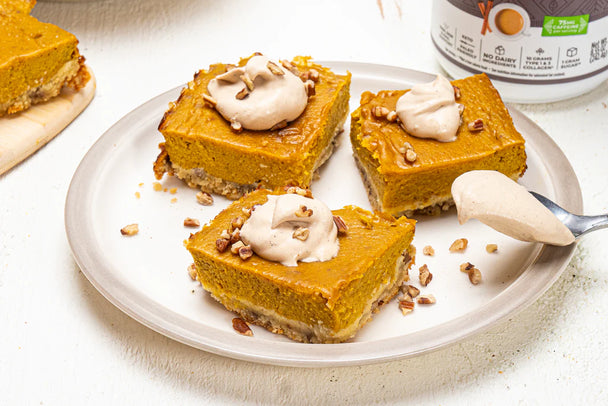 Three pumpkin pie bar squares topped with whipped cream, on a white plate, with a cream-coated spoon resting on the side..