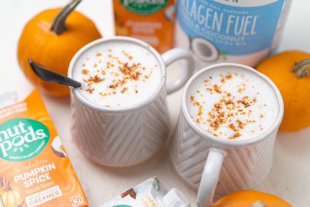 Two cups of pumpkin spice collagen latte surrounded by pumpkins, Primal Kitchen Collagen canister, and creamer.