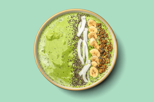 Overhead view of a green smoothie bowl topped with chia, banana, coconut, and granola. 