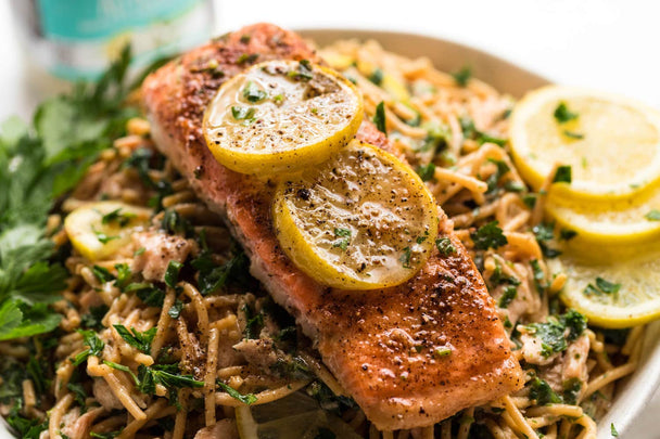 A bowl of chickpea spaghetti topped with baked salmon, with lemon slices for garnish.