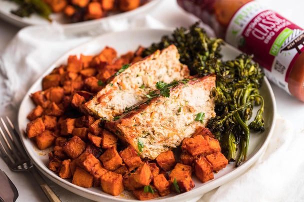 Turkey meatloaf slices, sweet potatoes, and greens on a white plate with a bottle of Classic BBQ Sauce in the background.