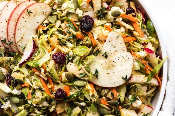 Closeup on a bowl of shaved Brussels sprout salad topped with apples, cranberries, and Primal Kitchen Honey Mustard Dressing.  