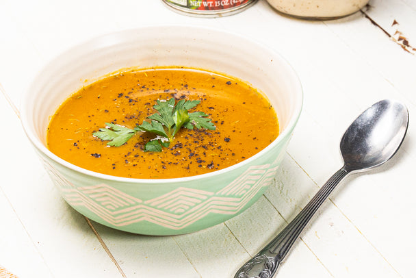 A bowl of creamy pumpkin soup next to a spoon.