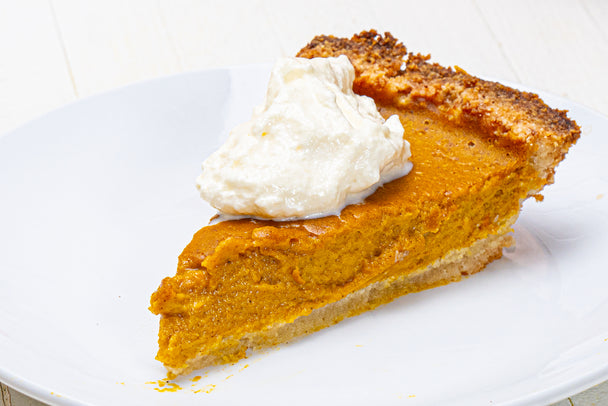 A slice of pumpkin pie topped with whipped cream on a white plate.