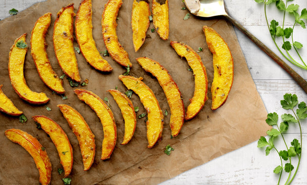 Two rows of cooked spicy pumpkin fries on a wooden cutting board.