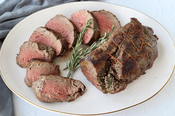 A beef tenderloin, partially sliced into thick slices, arranged in a circular pattern on a white platter.