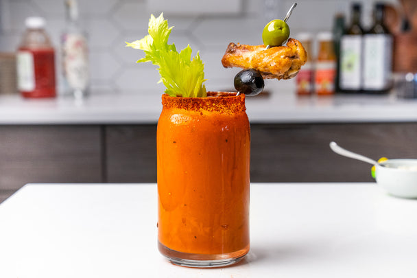 A Virgin Bloody Mary made with Primal Kitchen Buffalo Sauce, on a white kitchen countertop with other products in the background.