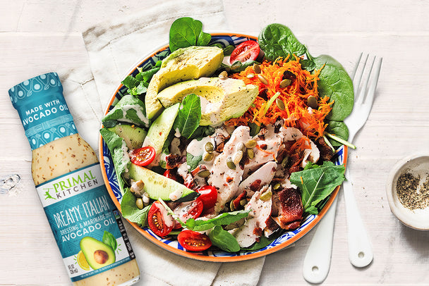 A grilled chicken salad in a bowl, next to a bottle of Primal Kitchen Dreamy Italian Dressing.