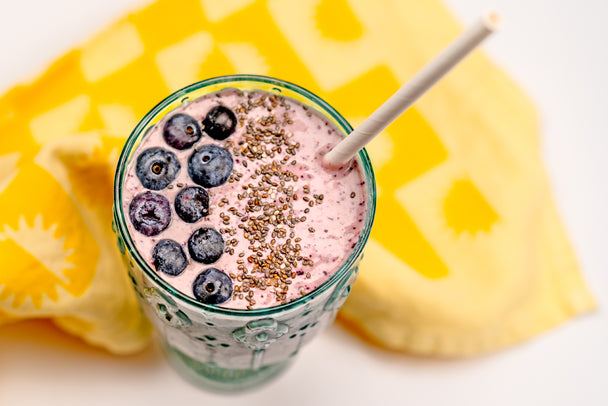 Closeup overhead shot of a Blueberry Muffin Smoothie with hemp seeds, next to a yellow printed linen napkin. 