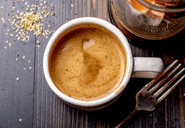 Overhead view of a vanilla collagen hemp latte, with a fork and a glass jar in the background.