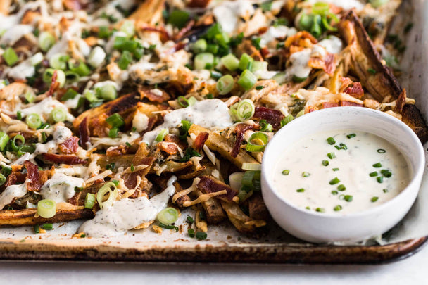 Closeup on a tray of Chicken Bacon Ranch Loaded Fries with a ramekin of Primal Kitchen Ranch.