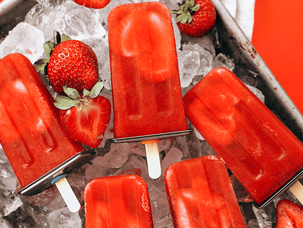 Strawberry orange collagen frozen pops over ice on a metal tray.