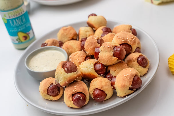 A plate of gluten-free pigs in a blanket with Primal Kitchen Ranch for dipping. 