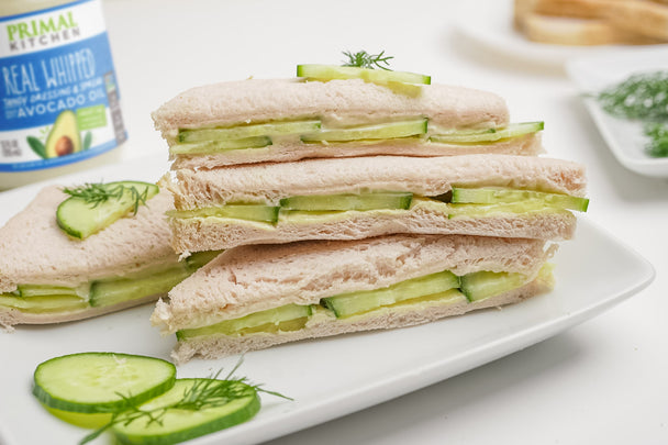 A stack of crustless cucumber sandwich triangles made with whipped spread, on a white plate.