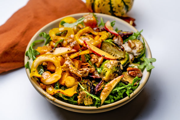 A Primal Harvest Bowl topped with honey mustard dressing. Rust colored napkin in background.