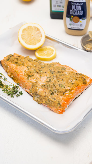 Baked salmon fillet covered with dijon mustard sauce on a baking sheet with fresh thyme and lemon. 