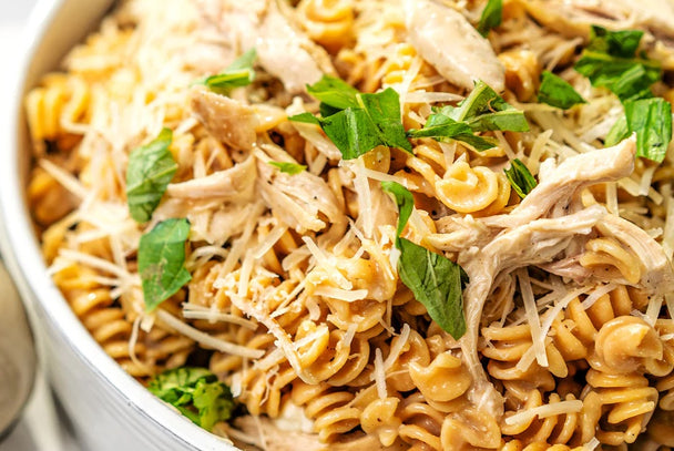 Close up shot of white bowl with fusilli pasta with chicken, shredded parmesan cheese, and fresh basil. 