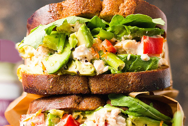 Close up shot of tuna salad sandwich loaded with avocado, red pepper, and leafy greens.