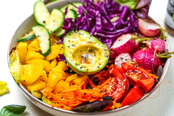 Colorful salad with bell peppers, cucumber, radishes, carrots, and half and avocado