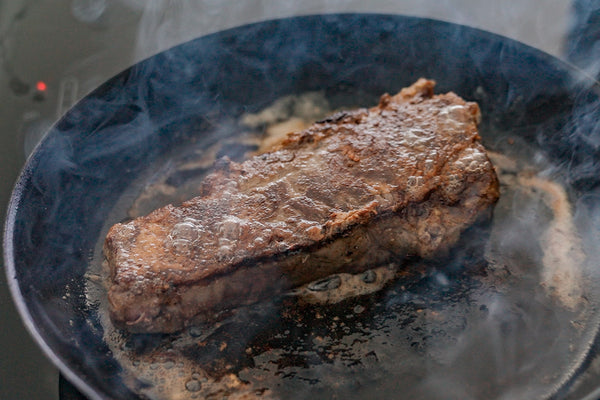 A pan-seared steak sizzling in a cast iron pan. 