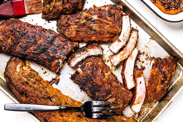 A tray of cooked baby back ribs with a fork. 