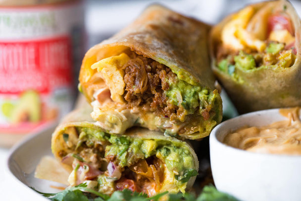 Stacked halves of a chorizo breakfast burrito on a plate with a small bowl of Primal Kitchen Chipotle Lime Mayo and a jar of mayo in the background.