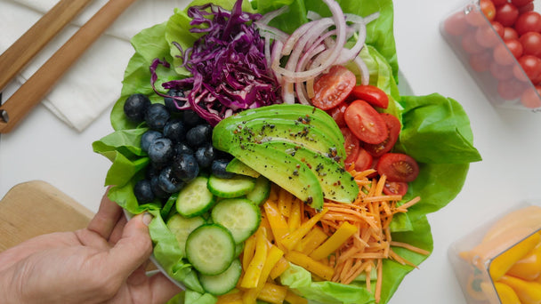  A hand holding a bowl of rainbow salad made with Primal Kitchen Balsamic Vinaigrette. 