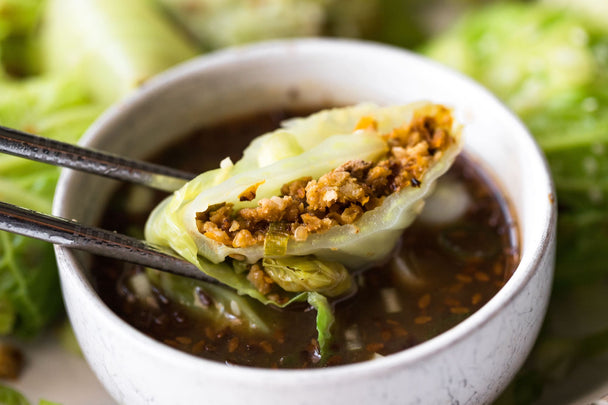 Chopsticks dipping an open pork and cabbage dumpling into a container of teriyaki sauce.