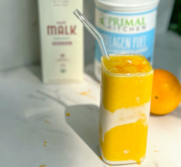 An orange cream smoothie in a glass with a straw. A canister of Primal Kitchen Collagen and a carton of Oat Malk in the background.