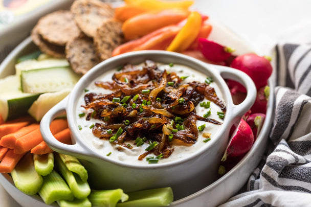  A ramekin of caramelized onion dip on a round platter with veggies and crackers.