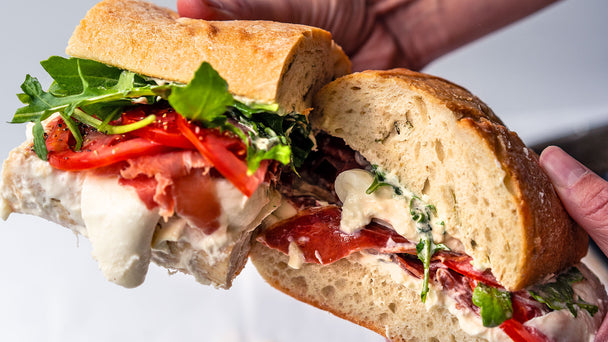 Hands holding two halves of a burrata caprese sandwich with gooey cheese oozing out.