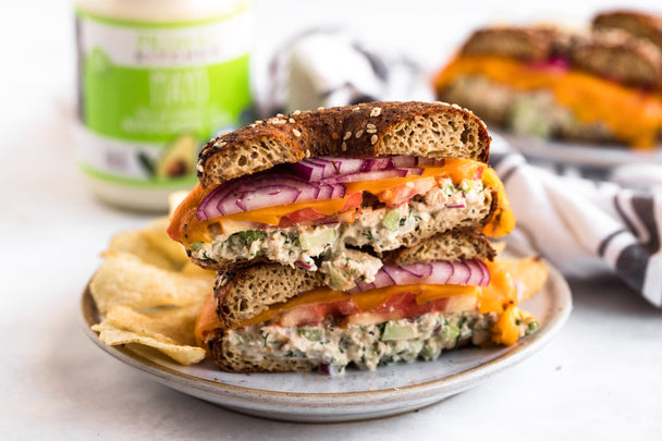 Two halves of a bagel tuna melt sandwich stacked on a plate with potato chips. 