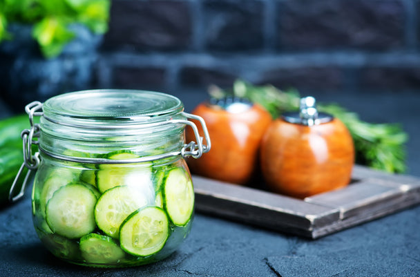 Thin-sliced cucumbers in a mason jar, with wooden salt and pepper shakers in the background.