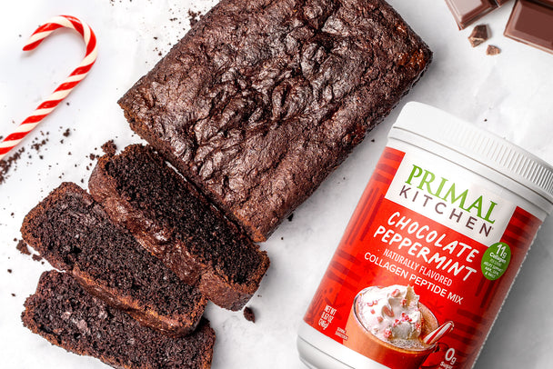 A chocolate peppermint loaf cut into slices, next to candy canes and a canister of Primal Kitchen Chocolate Peppermint Collagen. 