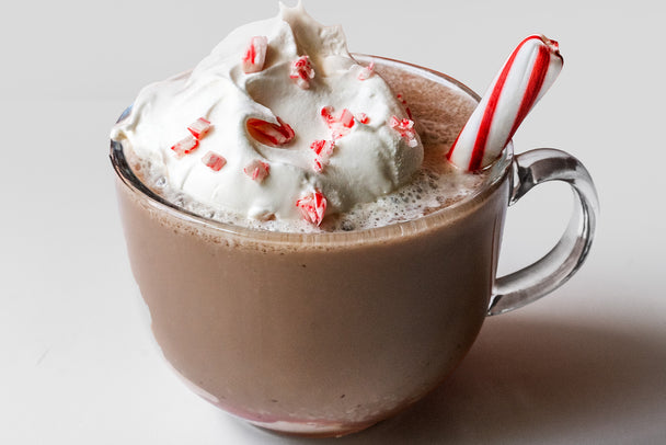 Peppermint hot chocolate garnished with candy cane pieces, in a clear glass mug.