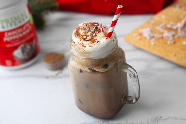 Iced peppermint mocha in a glass mug. A canister of Primal Kitchen Chocolate Peppermint Collagen in the background. 