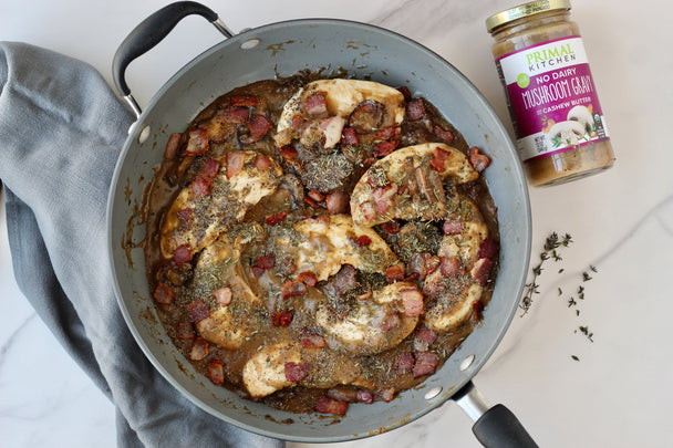 Chicken tenders with bacon and mushroom gravy in a skillet, next to a jar of Primal Kitchen Mushroom Gravy.