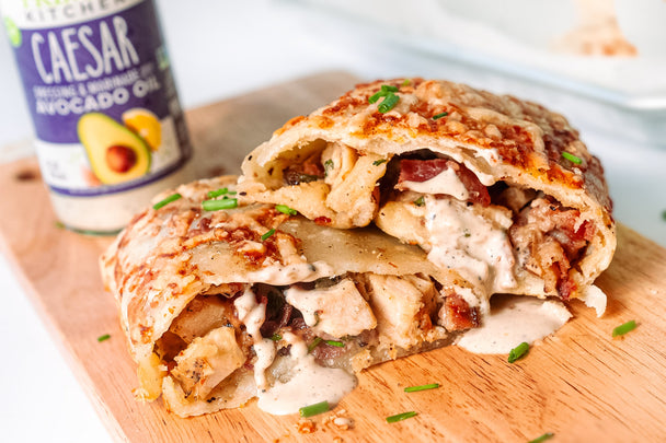 A chicken bake cut in half and stacked, on a cutting board, next to a bottle of Primal Kitchen Caesar dressing.