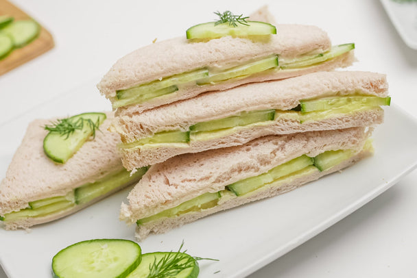 A stack of crustless cucumber sandwich triangles made with avocado oil mayo, on a white plate.